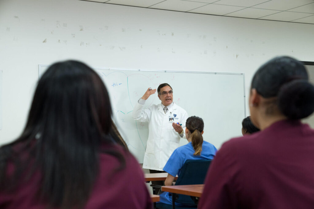 A Trained and Qualified Professor teaching a group of students in the classroom.Bay Area Medical Academy offers an accredited medical assistant program.