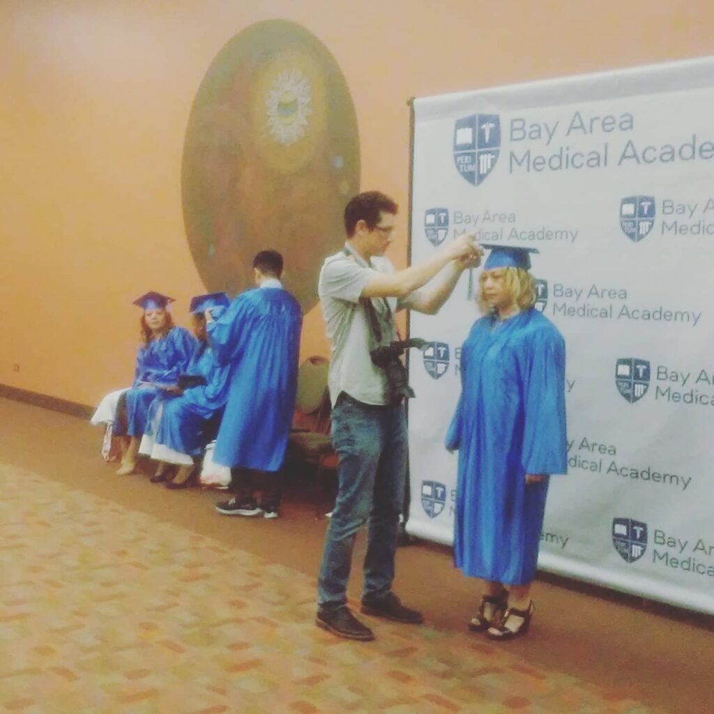 A Graduate standing towards the Bay Area Medical Academy Banner.
